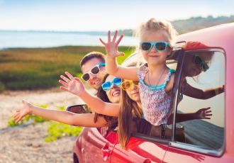 Ein Familie mit Sonnenbrillen winkt aus  dem Auto
